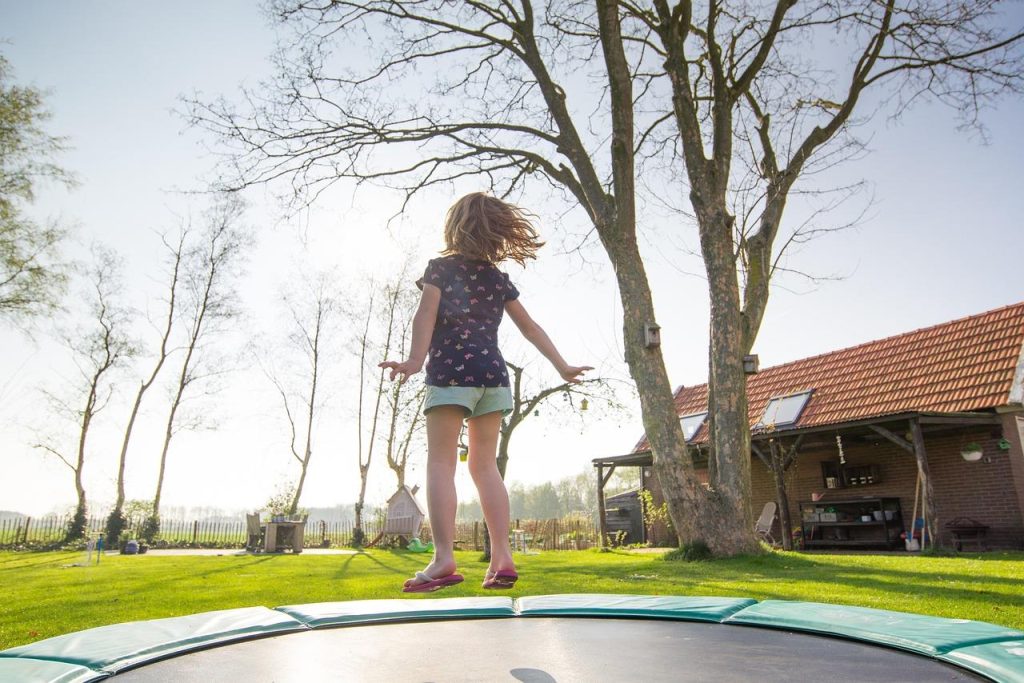 Familie geniet van trampolineplezier in de achtertuin met veiligheidsnet en randkussens voor veilig springen